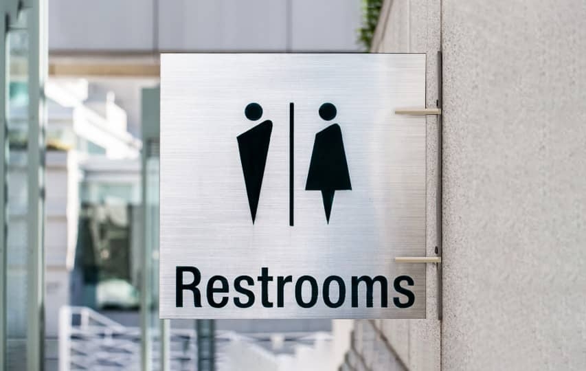 Brushed aluminum restroom sign with male/female icons and 'Restrooms' text mounted on wall