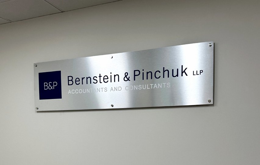 Brushed aluminum branding sign featuring the logo in black and reading the company's name.